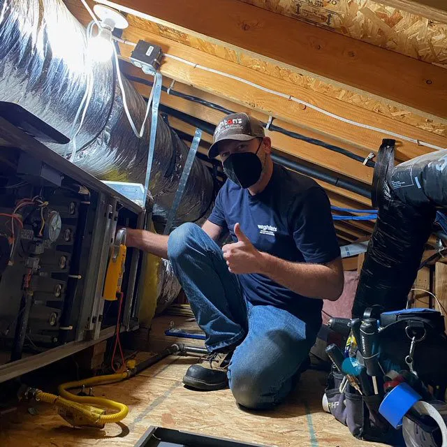 "A technician from Wightons Plumbing, Heating, & Air Conditioning working on HVAC systems in a San Luis Obispo attic. The individual is wearing a mask and giving a thumbs up."