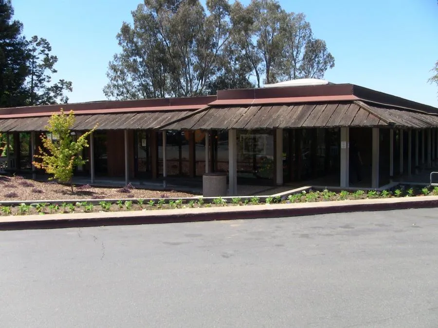 Exterior view of the William M. Schneider, D.D.S. dental office in Walnut Creek, featuring a modern, low-lying building with large windows and a wooden overhang surrounded by landscaped greenery.