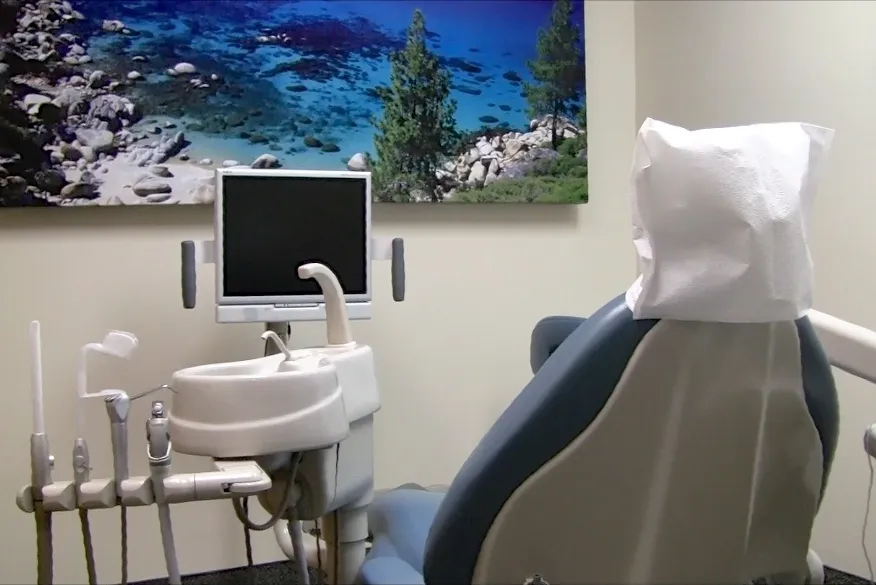 Dental office with a chair, dental tools, a monitor, and a scenic landscape picture on the wall.