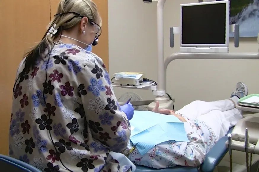 A dental professional attending to a patient in a dental office at William M. Schneider, D.D.S. in Walnut Creek, with medical equipment visible in the background.