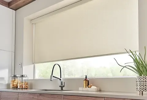 A modern kitchen window with a sleek, rolled-down blind above a sink, decorated with a soap dispenser and a plant.