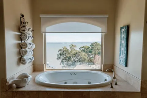 Luxurious bathtub facing a large window with a scenic view of trees and water, enhanced by Window-ology's custom window treatments in Pleasanton.