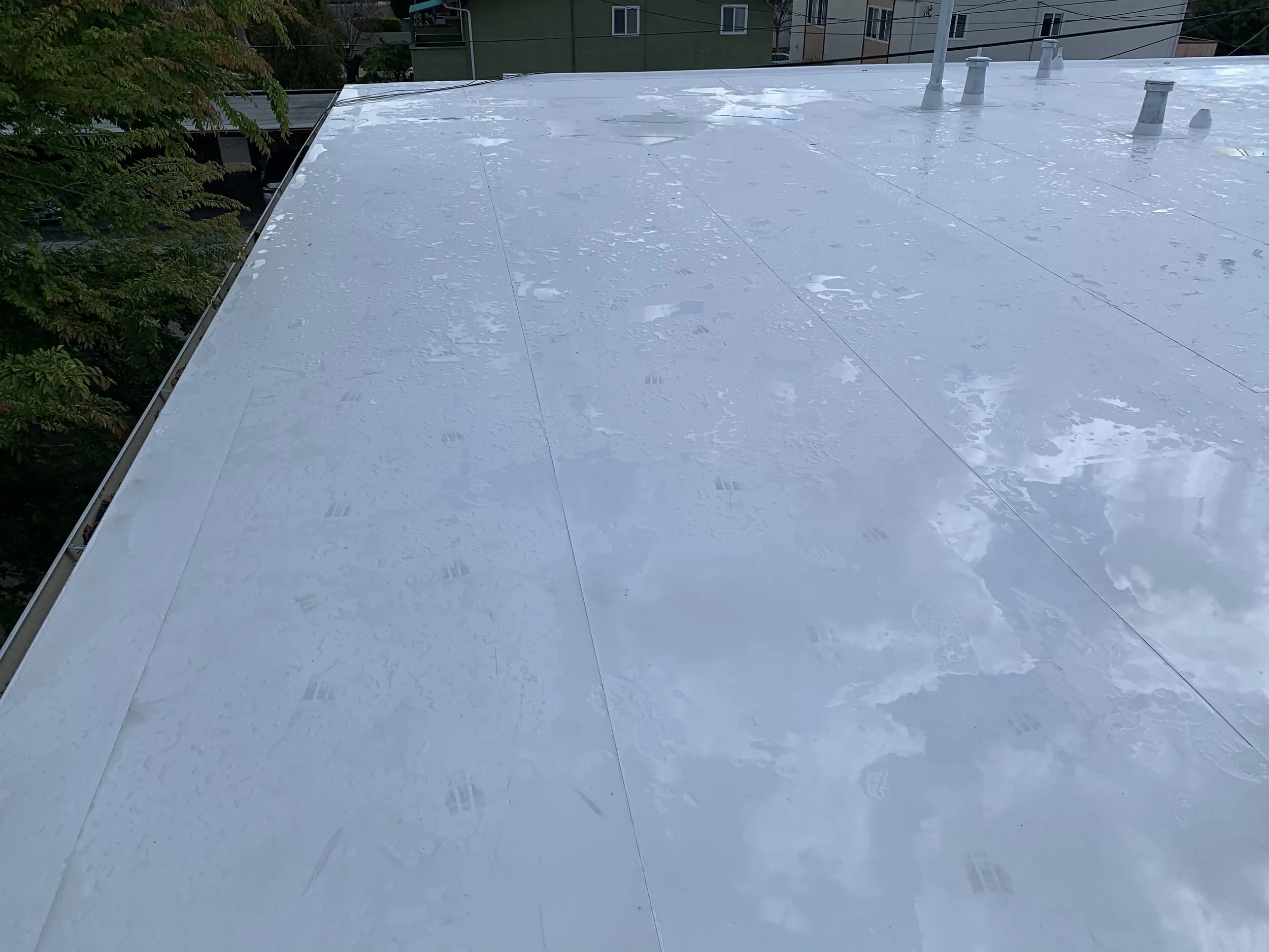 A flat, white roof surface showing signs of wear and water pooling, installed by Winter Roofing Inc. in Morgan Hill.