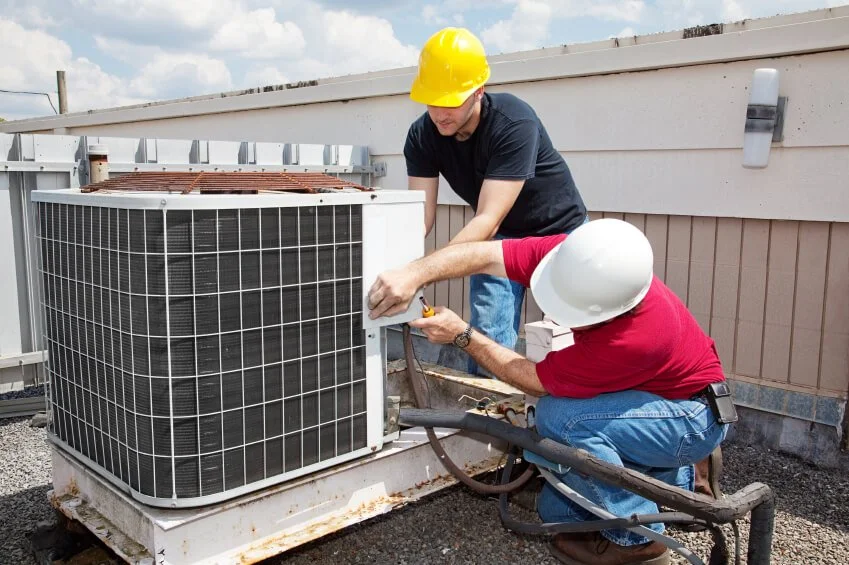 Two HVAC technicians in hard hats service a rooftop air conditioning unit, representing A-1 Guaranteed Heating & Air, Inc. of Novato, CA performing maintenance to ensure system efficiency and safety.
