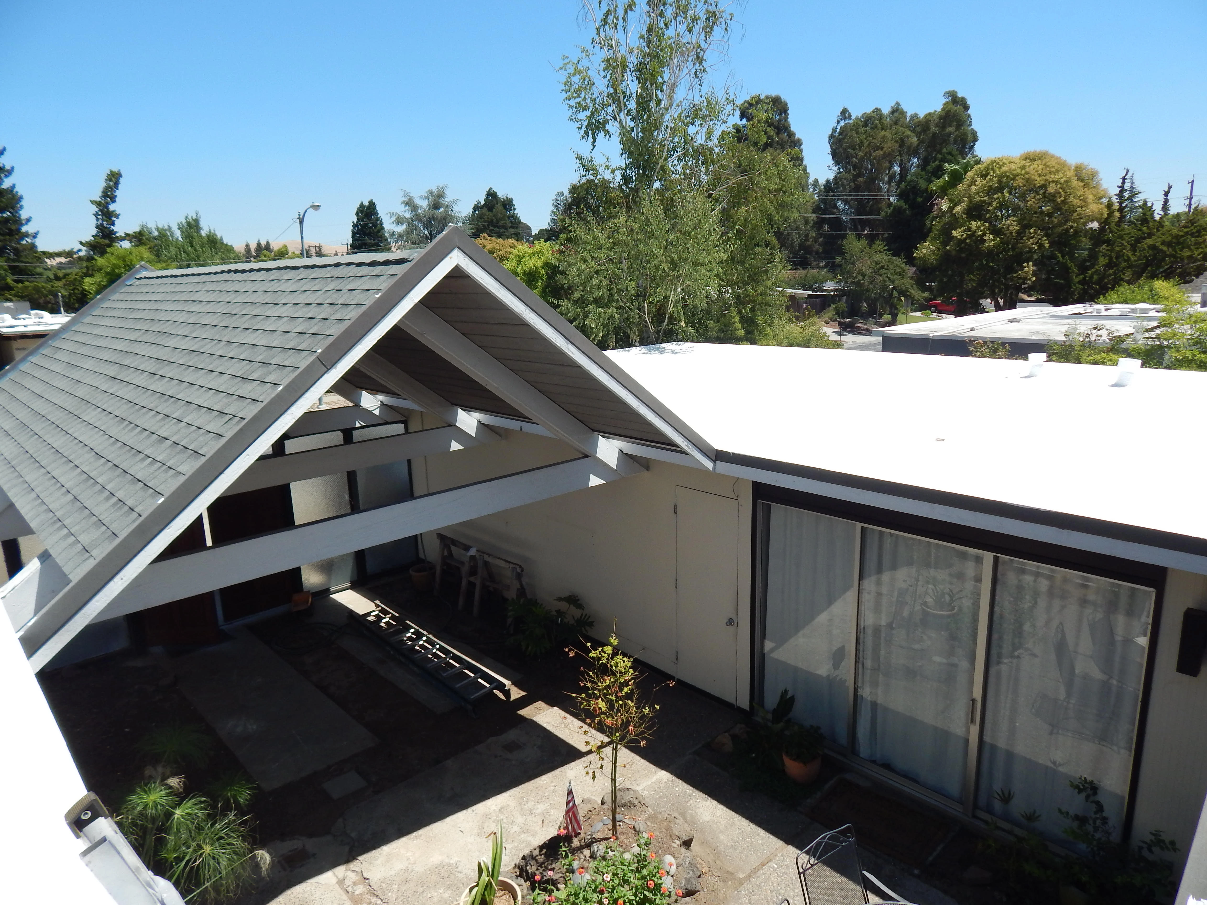 A residential home featuring a white flat roof and an adjacent pitched shingle roof, surrounded by trees and visible under a clear sky, illustrating roofing work by Abril Roofing, Inc. in Martinez, CA.