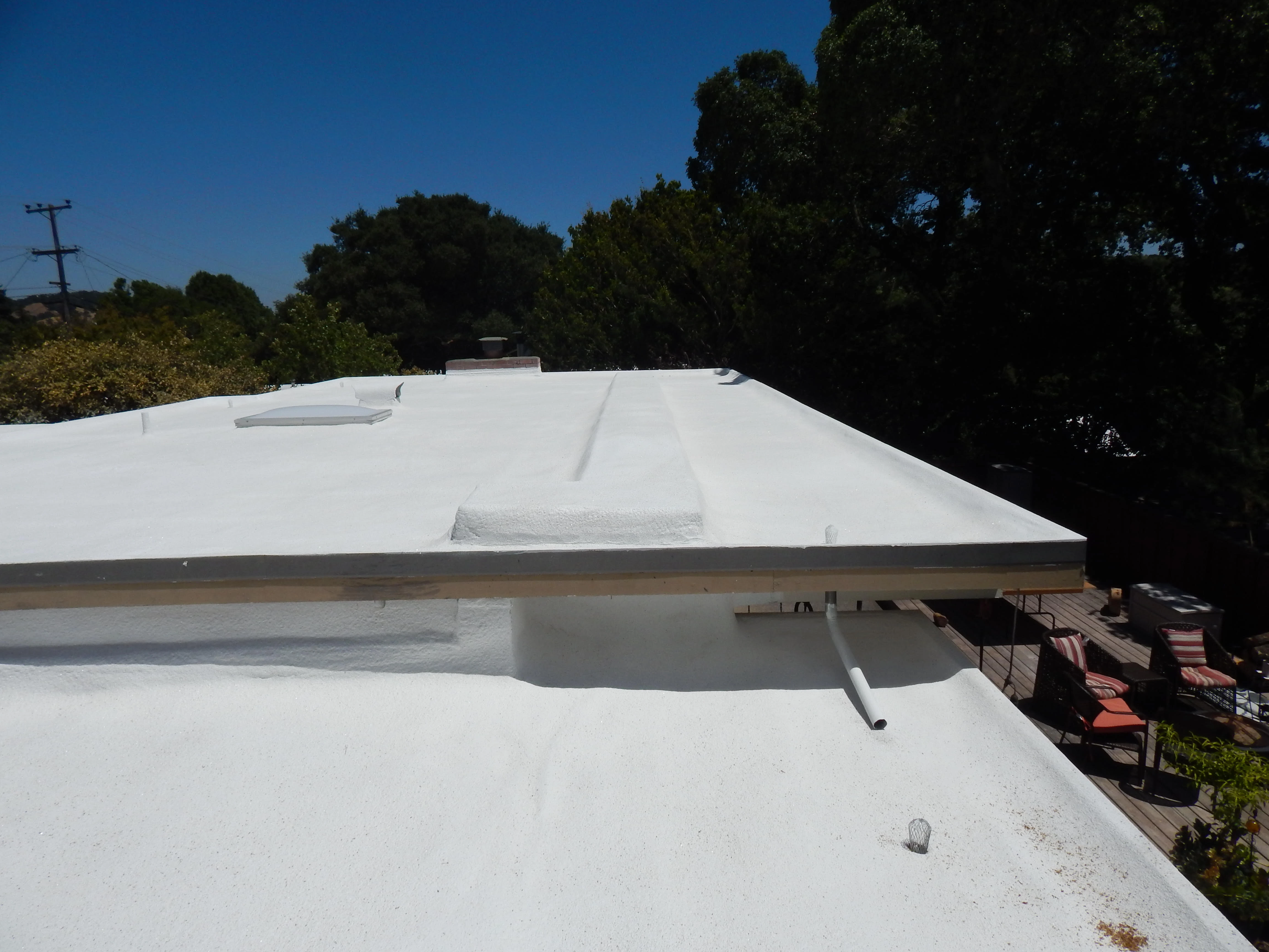 A white flat roof with a small skylight and drainage pipe, surrounded by trees and a patio area, showing energy-efficient roofing work by Abril Roofing, Inc. in Martinez, CA.