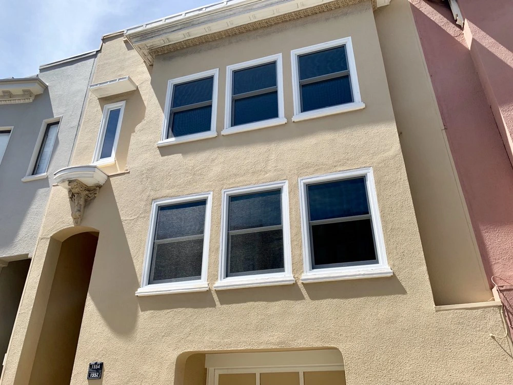 A beige multi-story residential building with six newly installed rectangular windows featuring white trim, demonstrating retrofit window work by Abstract Windows in San Carlos, CA.