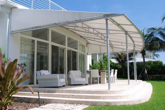 A modern curved metal-framed patio cover with white fabric shading a rounded stone patio and white outdoor furniture, installed by Acme Sunshades Enterprise Inc. in Hayward, CA.