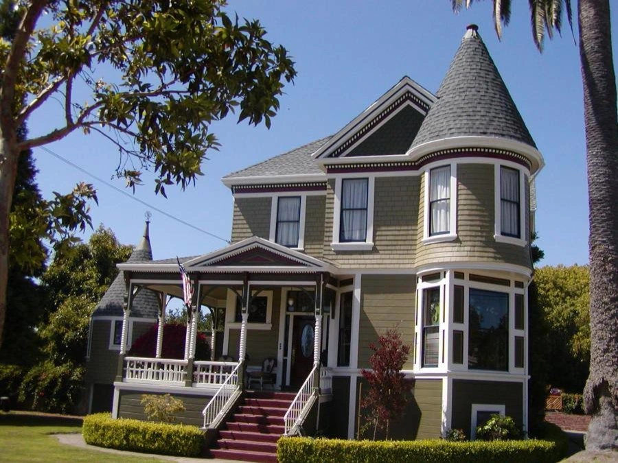 A classic Victorian-style house with a complex, multi-pitched roof and turret, restored with precision shingle roofing by Advanced Roofing Services, Inc. in Alameda, CA, surrounded by trees and a manicured lawn.